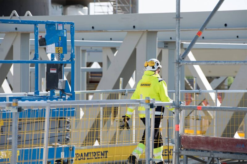 Työvaatteisiin pukeutunut henkilö kävelee suojakaiteiden takana työmaalla.