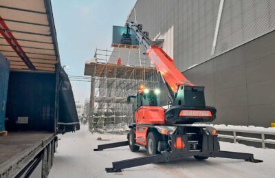 Punainen kurottaja nostaa urheiluhallin seinän vieressä levyä auton perästä telineellä työskentelevälle henkilölle.