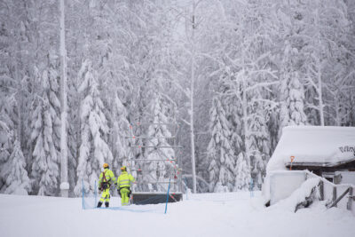 Kaksi huomiovärivaatteisiin pukeutunutta henkilöä kasaa telinettä lumisessa maastossa.