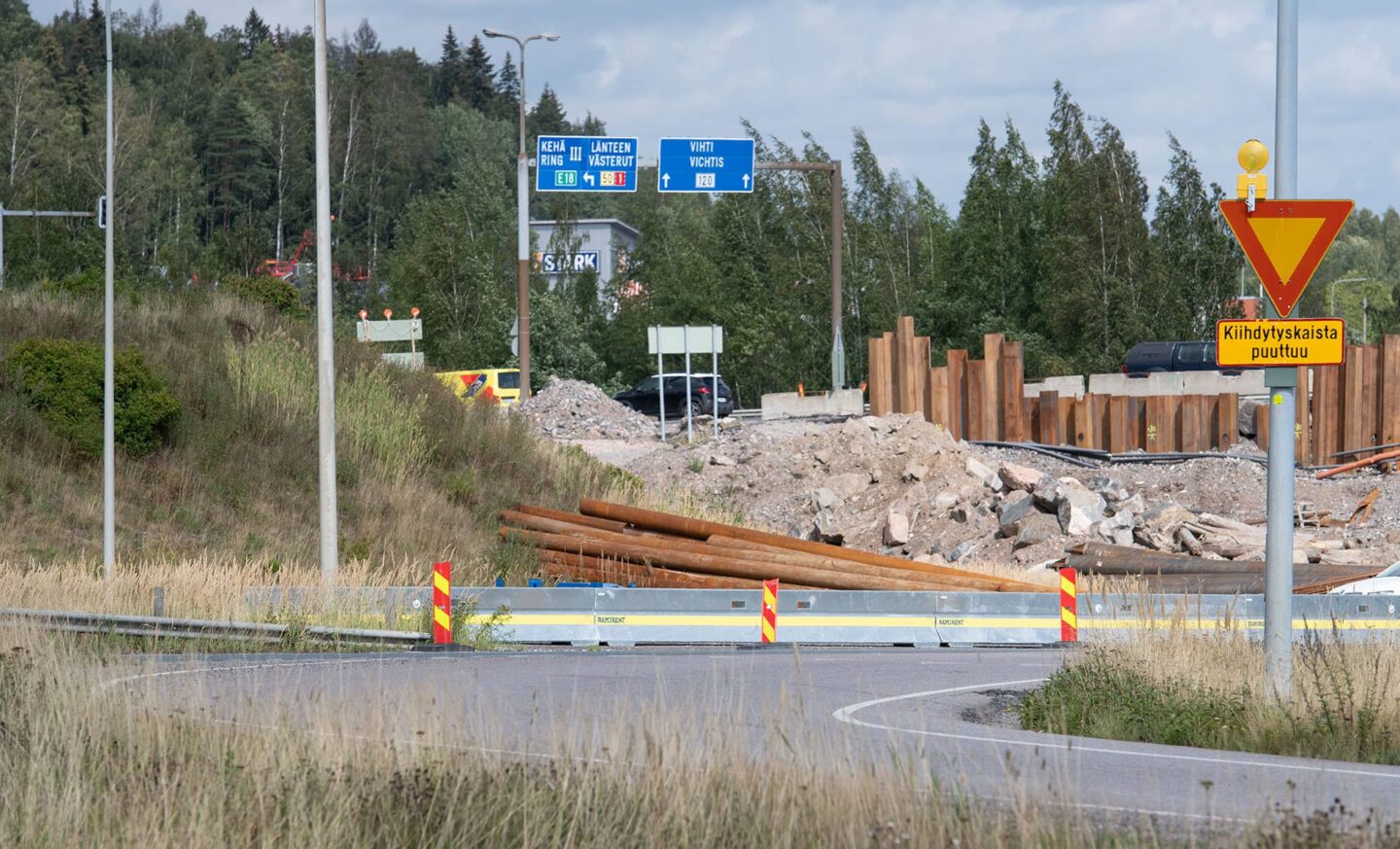 Tien mutka joka on suojattu liikennekaiteella ja sulkulamelleilla.