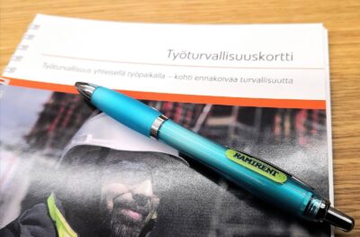 Pöydällä oleva vihko, jonka otsikkona on työturvallisuusvihko ja päällä on kuulakärkikynä.